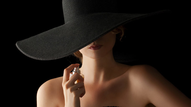 帽子をかぶった香水を体につける女性