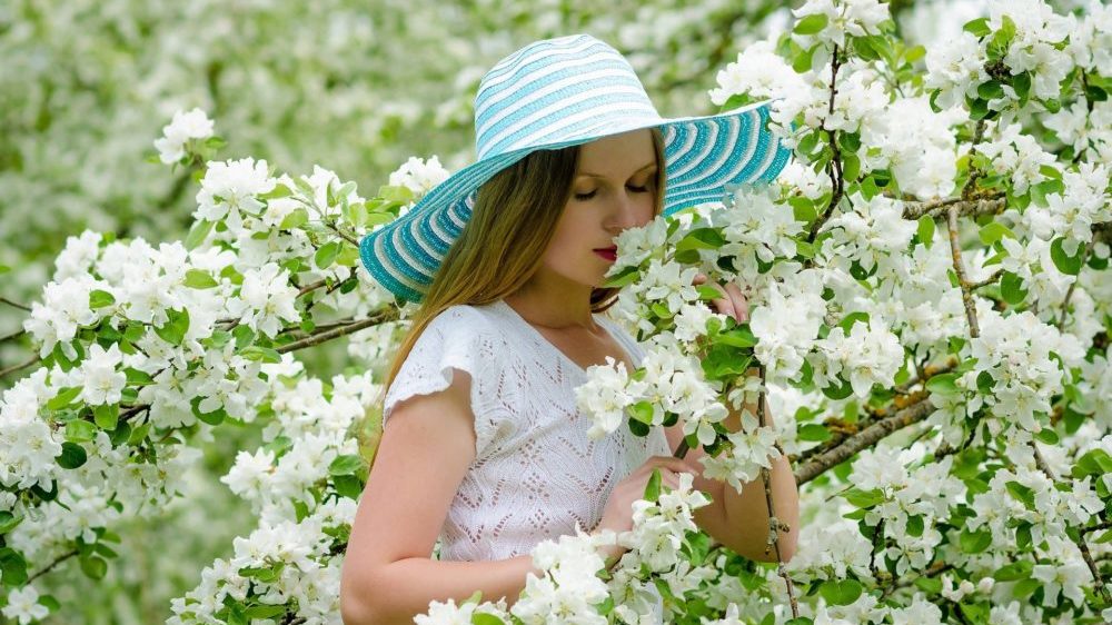 白い花を嗅ぐ、帽子をかぶった女性