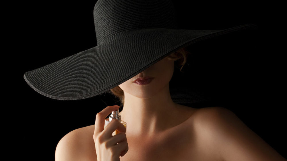 黒い背景で香水を使うエレガントな女性